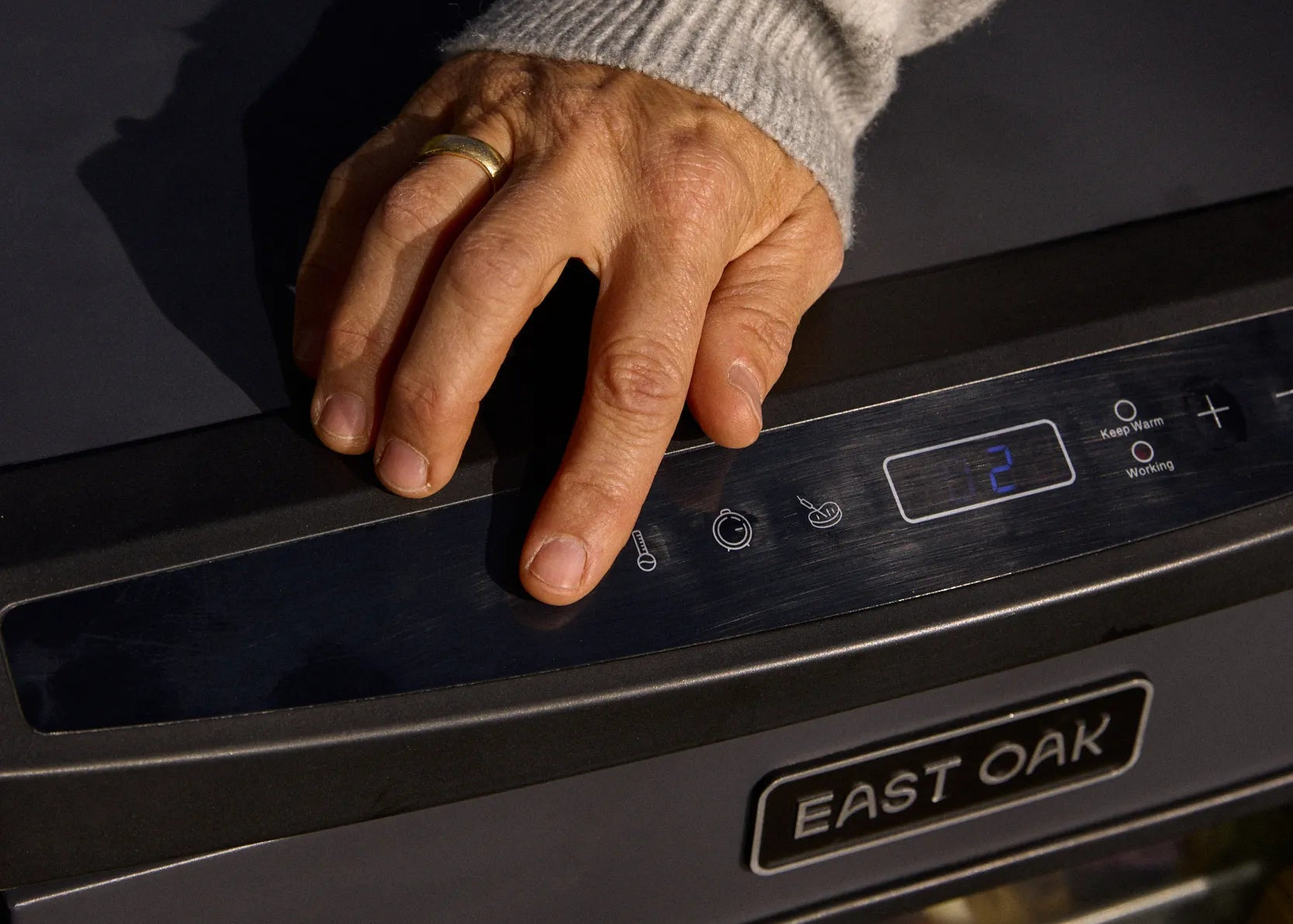 Person's hand reaching towards an East Oak oven with a blurred background